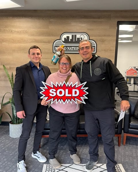 Three people holding a red SOLD sign in a real estate office
