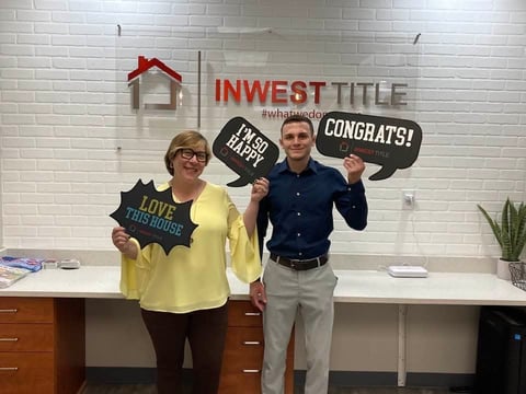 Two people holding speech bubble props at Invest Title office, celebrating with congratulations signs