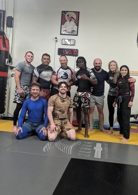 Group of people in martial arts uniforms and casual clothes posing together on a gym mat
