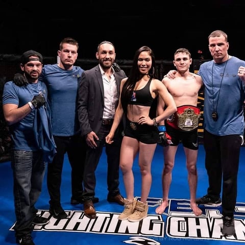 Group of six people posing on boxing ring stage, with two athletes wearing championship belts standing center