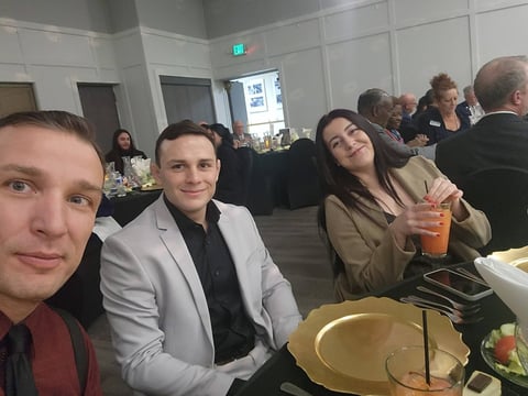 Four people seated at a dining event in a modern venue with gold plates and beverages