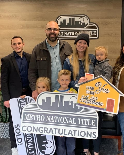 Family celebrating real estate sale with Metro National Title banner and sold sign at closing office