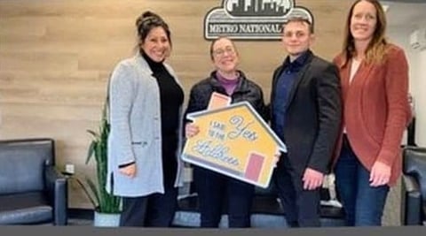Four people standing in front of a Metro National sign, holding a yellow house-shaped award