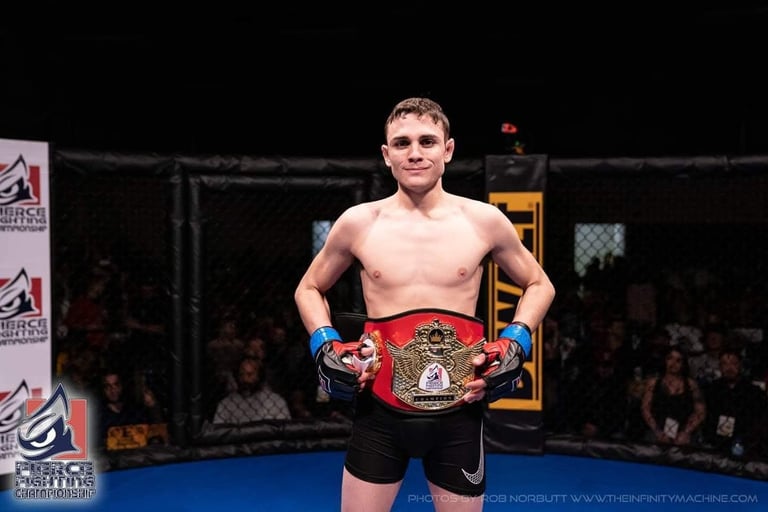 Shirtless male fighter wearing championship belt standing in boxing ring during victory pose with crowd in background