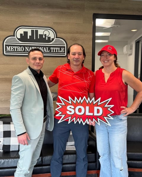Three real estate professionals holding a red SOLD sign at Metro National Title office